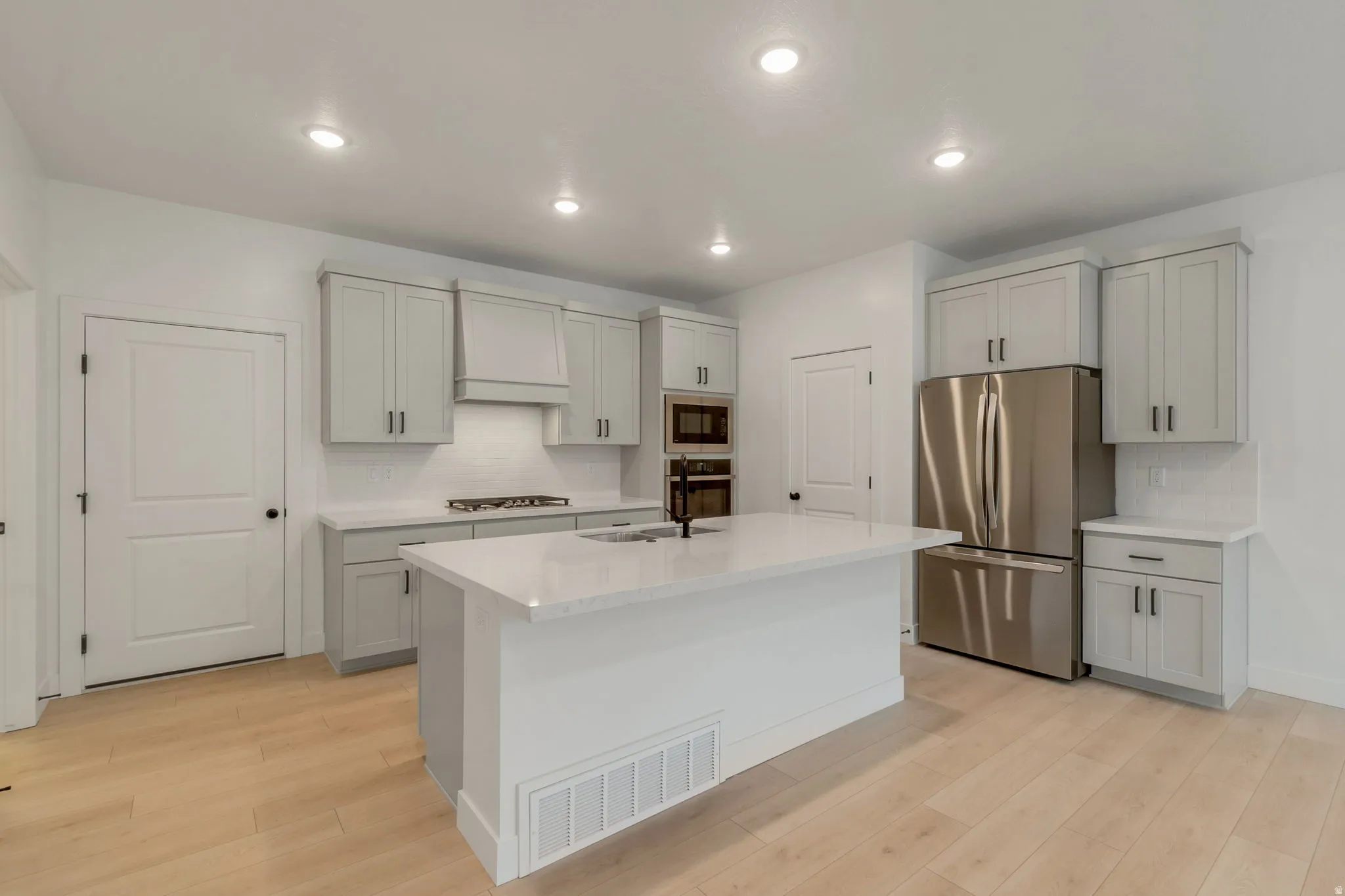 Modern kitchen featuring light wood-finish flooring, white walls, recessed ceiling lighting, and a kitchen island with a built-in sink