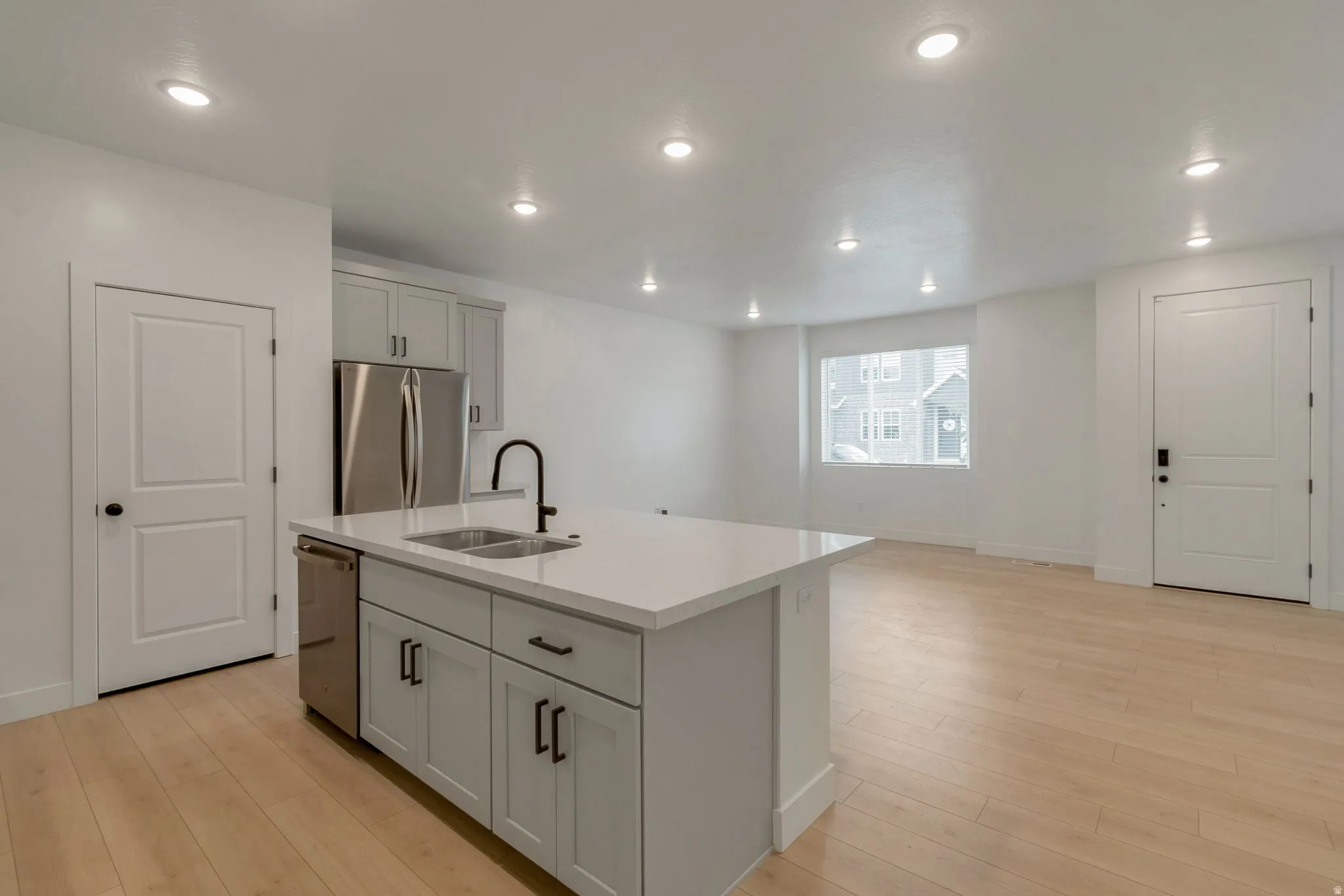 Kitchen island with an undermount double-basin sink and matte black faucet, light wood-finish flooring, recessed lighting, and stainless steel appliances