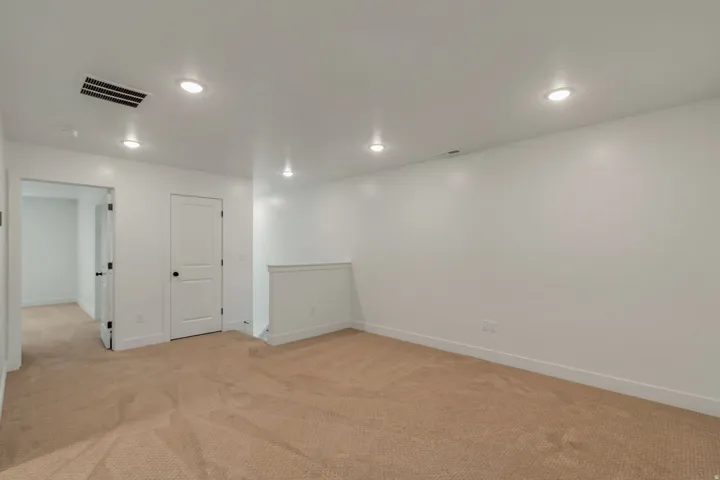 Spacious open area on upper floor, perfect for office, gym or play area. Featuring neutral carpeting, white painted walls, and recessed lighting