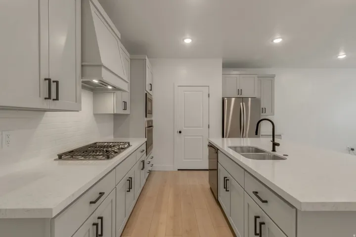 Modern kitchen featuring light-toned cabinetry with dark hardware, a center island with an undermount sink and matte black faucet, and light wood-finish flooring