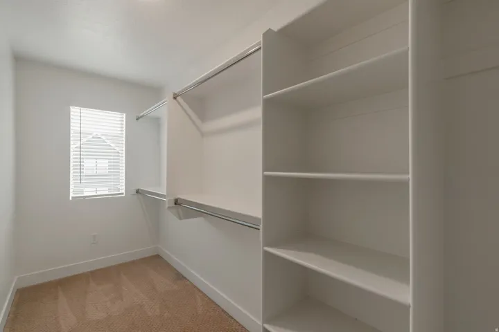Walk-in closet featuring built-in shelving, dual hanging rods, and a window with blinds