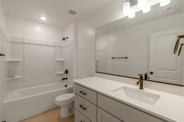 Bathroom featuring a single vanity with an integrated sink and white countertop, bronze-finish fixtures, a full-width mirror, and a white tub/shower combination