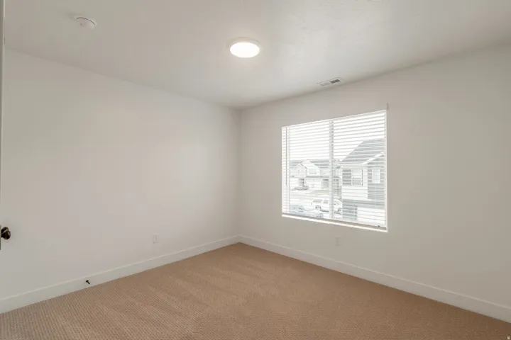 Room featuring light beige carpeting, white walls, a single window with horizontal blinds, and a flush-mount ceiling light