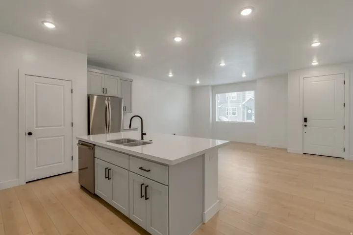 Kitchen island with an undermount double-basin sink and matte black faucet, light wood-finish flooring, recessed lighting, and stainless steel appliances