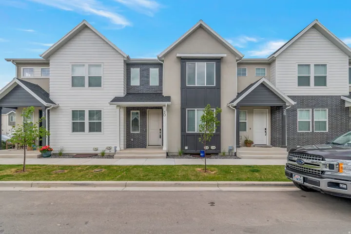 Modern townhome featuring a multi-textured facade with white siding, dark gray brick, and light stucco