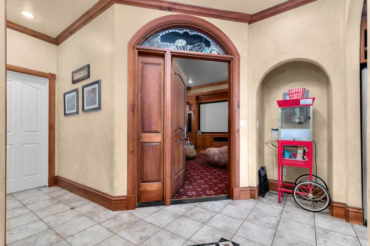 Arched entryway into theater room featuring custom wood double doors with an arched transom, tile flooring, and custom wood trim.