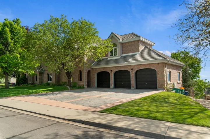 Brick exterior home featuring a three-car garage, tile roofing, and a patterned paver driveway
