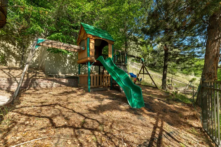 Outdoor play structure featuring a wooden playset with a green slide, an elevated fort, and an attached swing set