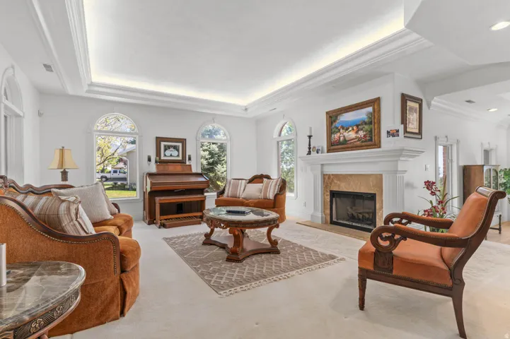 Living area featuring a tray ceiling, arched windows, a fireplace with a stone surround, and light-toned carpeting