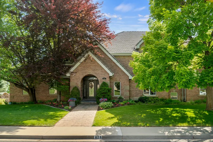 Brick exterior with arched entryway, a paver walkway, mature trees, and a well-maintained lawn
