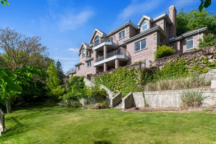 Expansive terraced property featuring a brick exterior, multiple balconies with metal railings, a manicured lawn, and mature trees