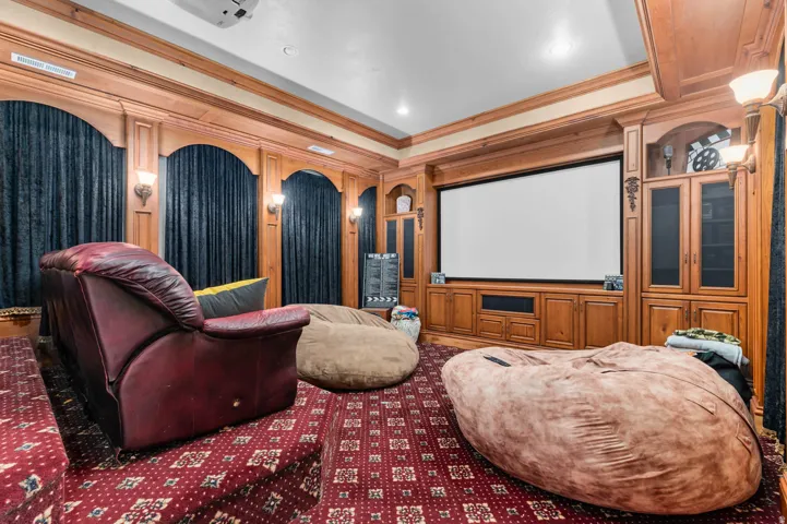 Dedicated media room featuring a large projection screen, built-in wooden cabinetry, custom wood paneling, recessed lighting, and sconce lighting