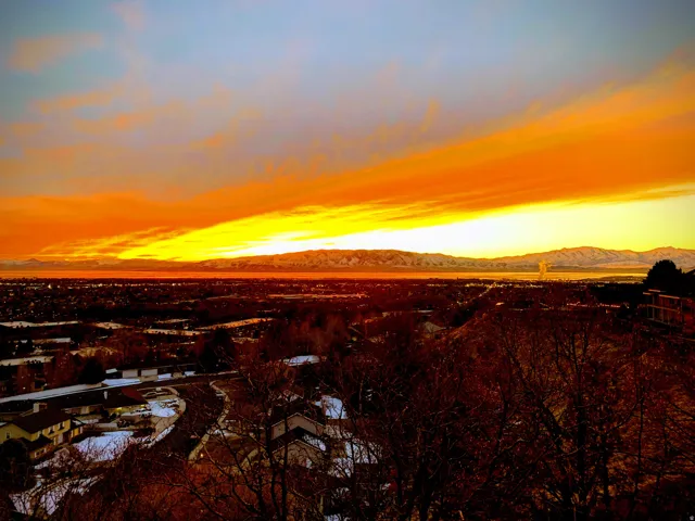 Expansive panoramic landscape featuring a prominent mountain range with snow-capped peaks, a large body of water, and a wide-ranging urban development