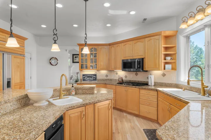 Light wood cabinetry and granite countertops define this kitchen, featuring a built-in microwave, gas cooktop, and gold-finish fixtures