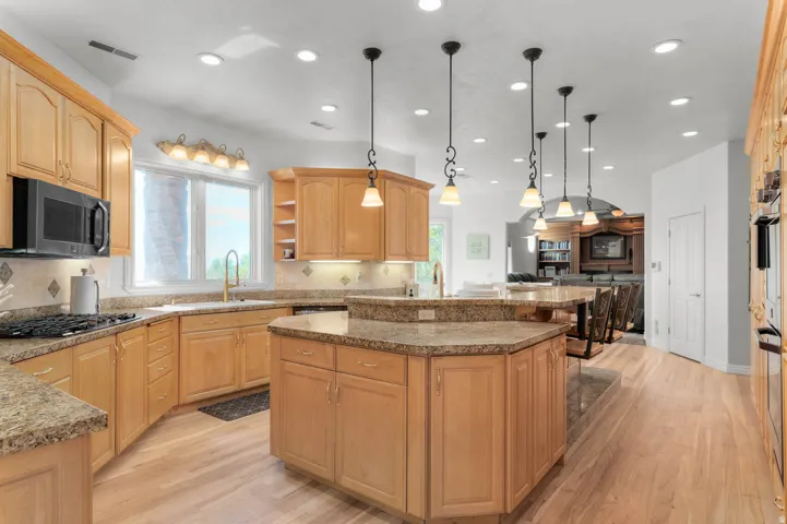 Expansive kitchen featuring light wood cabinetry, stone countertops, a large island with seating, a built-in microwave, and recessed lighting