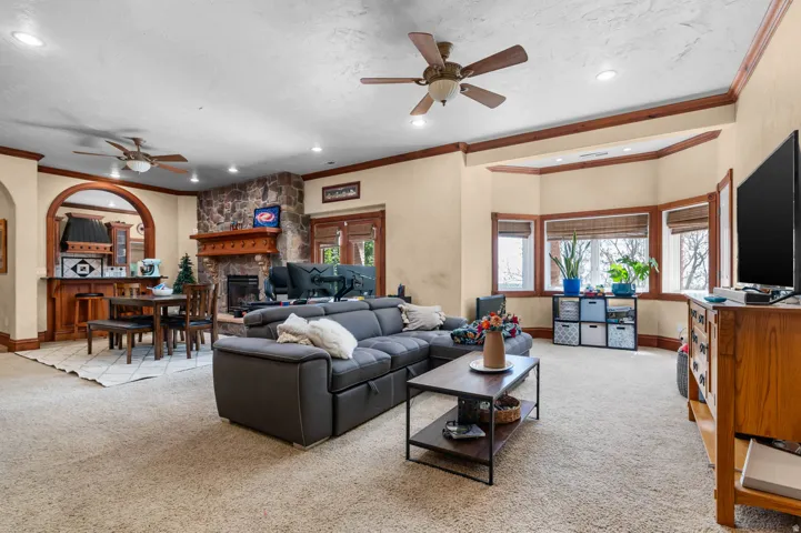 Carpeted living space featuring a stone fireplace with a wood mantle, a built-in wet bar with wood cabinetry, and a bay window