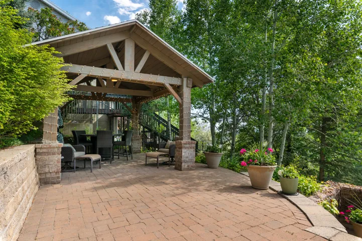 Expansive paver patio featuring a covered outdoor entertaining area with exposed beam ceilings and brick-clad columns