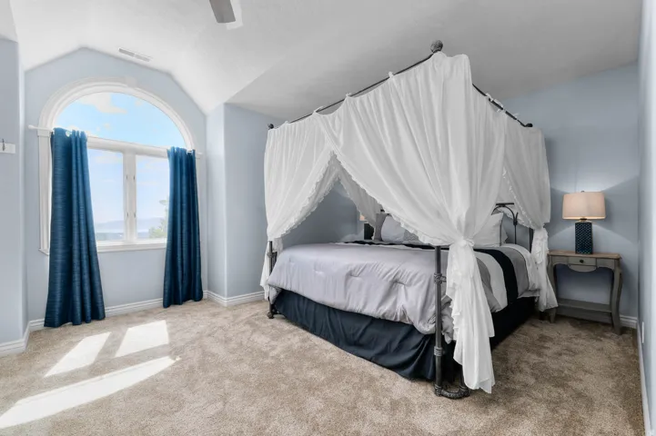 Arched window with broad sill, vaulted ceiling, light-toned carpet, and ceiling fan