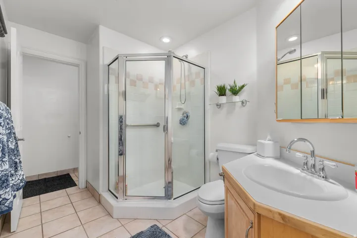 Bathroom featuring a corner glass-enclosed shower with tiled walls, a single vanity with a laminate countertop, and light-toned floor tiles