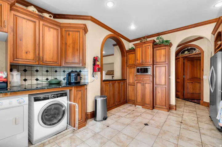 Kitchen featuring extensive wood cabinetry, tile flooring with diamond accents, dark granite countertops, and a patterned tile backsplash