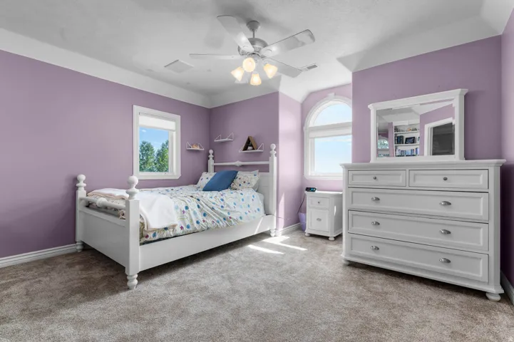 Carpeted interior space featuring a ceiling fan with integrated lighting, a rectangular window, and a prominent arched-top window