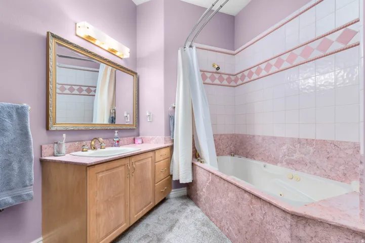 Bathroom featuring a vanity with wood cabinetry and a light-toned countertop, an undermount sink with a brass-finish faucet, and a large framed mirror