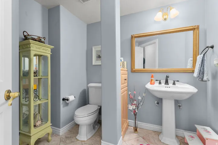 Pedestal sink with dark-finished faucet, illuminated by a three-light vanity fixture