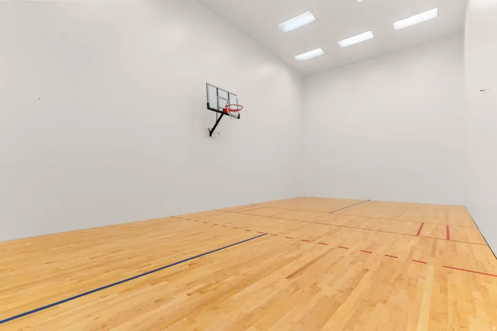Indoor court featuring wood-finish flooring with marked lines, a wall-mounted basketball hoop, and recessed ceiling lighting
