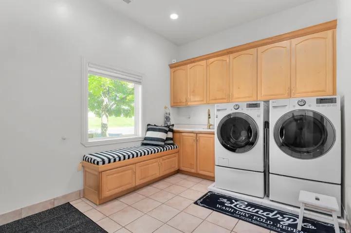 Dedicated laundry space featuring a built-in window seat, abundant cabinetry, ceramic tile flooring, and a utility sink
