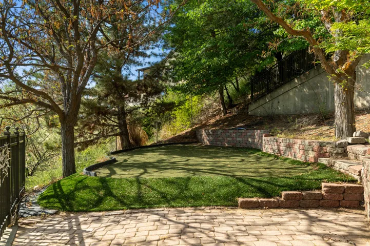 Outdoor space featuring an artificial turf putting green, paver patio, brick retaining walls, and mature trees