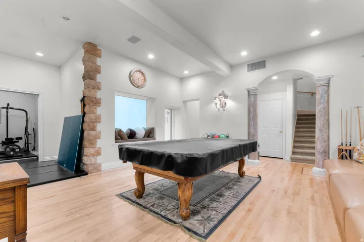 Recreation room featuring light wood-finish flooring, recessed lighting, and an arched entryway with decorative columns