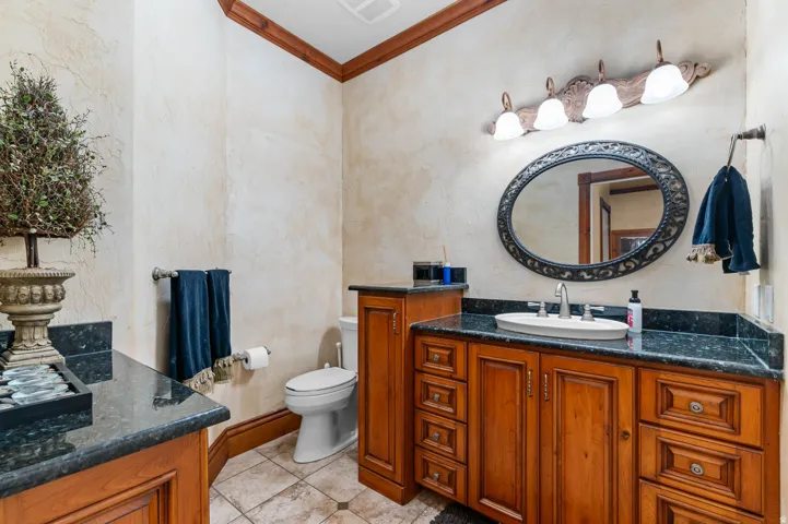 Bathroom featuring a wood vanity with a dark countertop, an oval-framed mirror, and a decorative light fixture next to theater room.