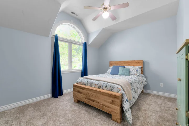 Room featuring a large arched window, vaulted ceiling, and ceiling fan with integrated lighting