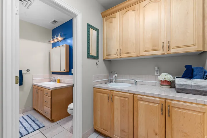 Utility room with extensive wood-finish cabinetry, a tiled countertop, and an integrated sink. Stackable laundry hook ups.
