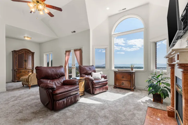 Spacious room featuring vaulted ceilings, a large arched picture window, multiple additional windows, a built-in fireplace with a stone mantel, and a ceiling fan with integrated lighting