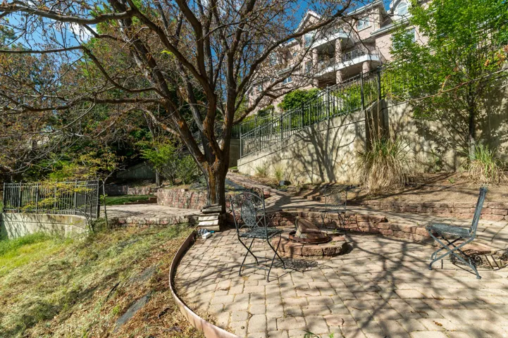 Brick paver patio with a built-in stone fire pit, surrounded by tiered landscaping and a retaining wall