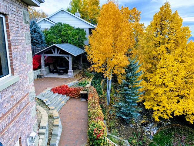 Brick and stone exterior featuring a multi-level paver patio, covered stone gazebo, terraced landscaping, and mature trees