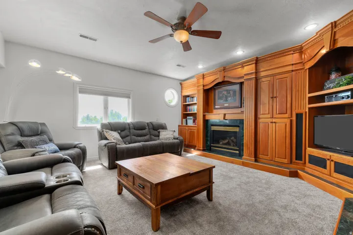 Living space featuring extensive built-in custom wood cabinetry and shelving, a central fireplace with dark stone surround, recessed lighting, and soft carpet flooring
