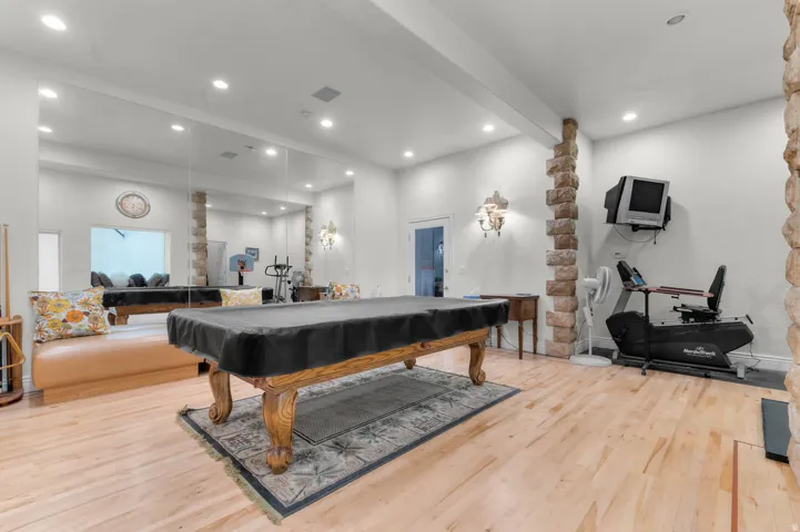 Spacious recreation room featuring light wood-finish flooring and extensive mirrored walls that could be used for a dance area.