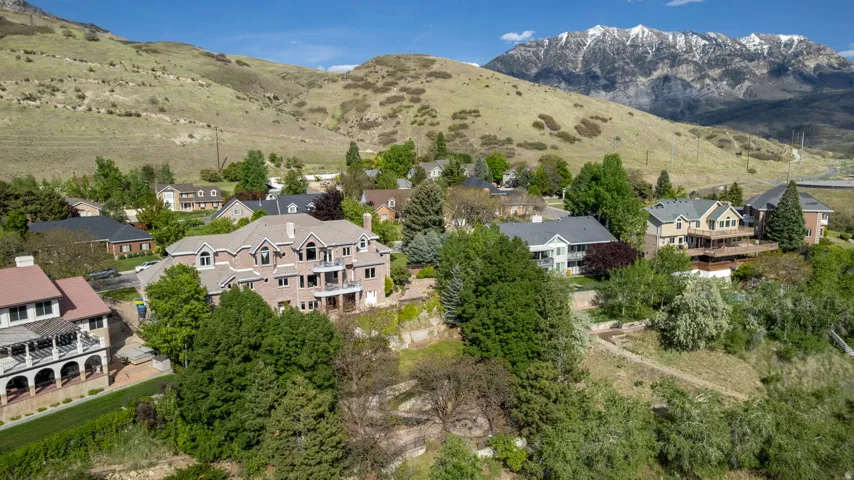 Expansive property featuring a brick facade, multiple balconies, a terraced landscape, a mature tree canopy, and a mountain backdrop