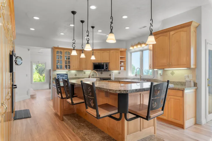 Expansive kitchen featuring a large central island with seating, natural wood cabinetry, recessed lighting, and granite countertops