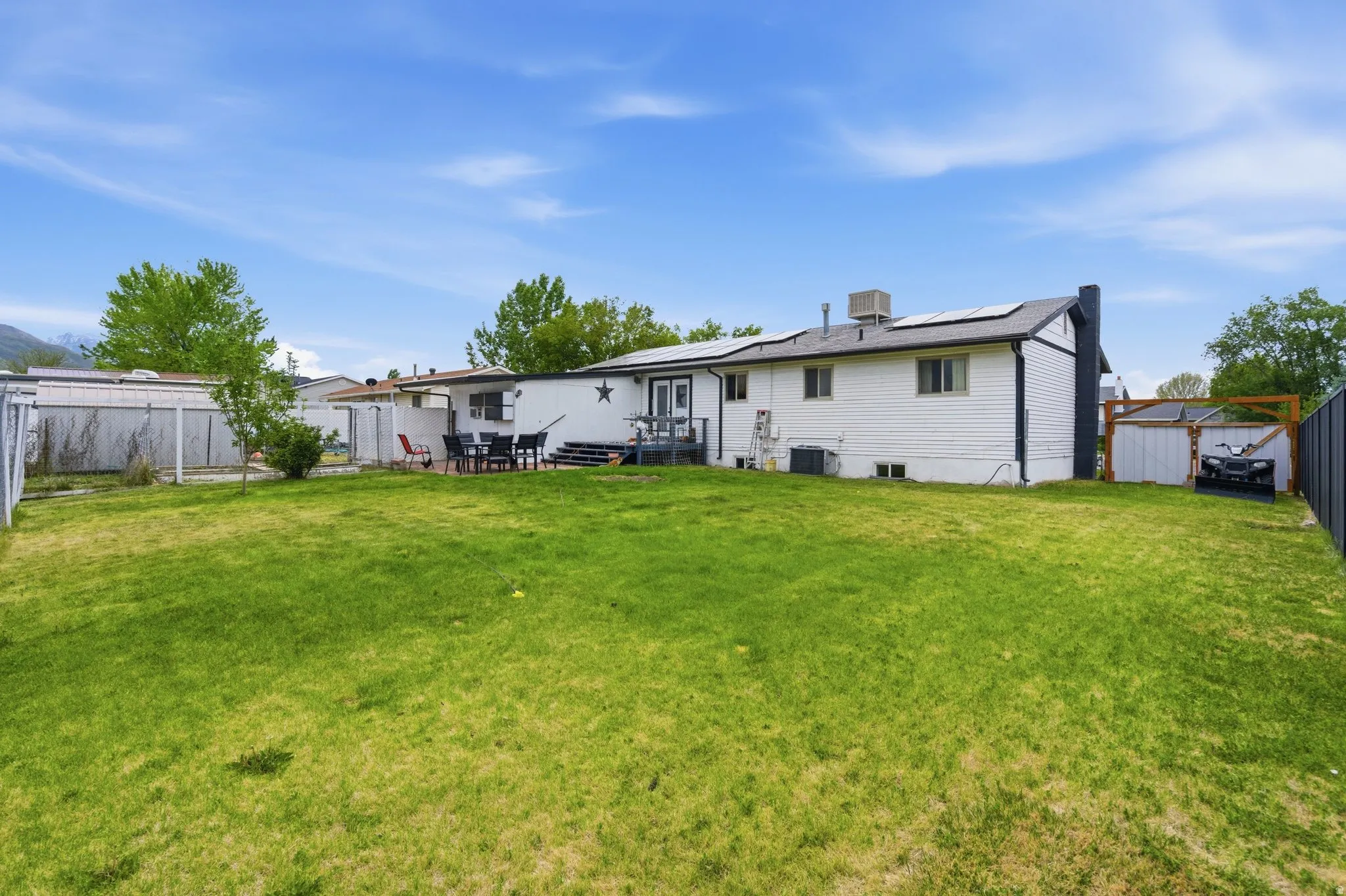 Expansive green lawn with a white exterior home featuring a rear deck, solar panels on the roof, and a privacy fence