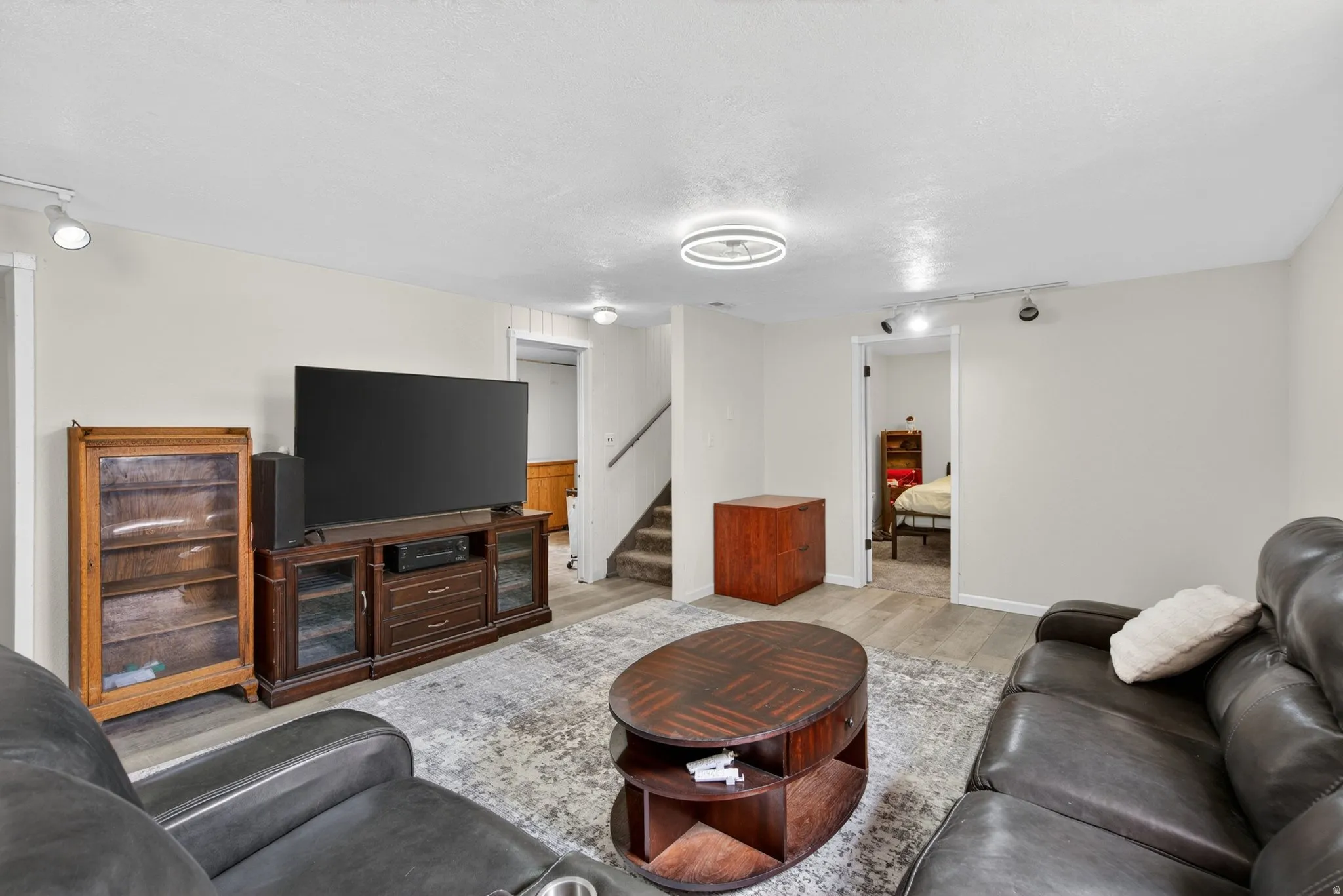 Spacious living area featuring light-toned walls, wood-finish flooring, a contemporary ceiling light fixture, and track lighting