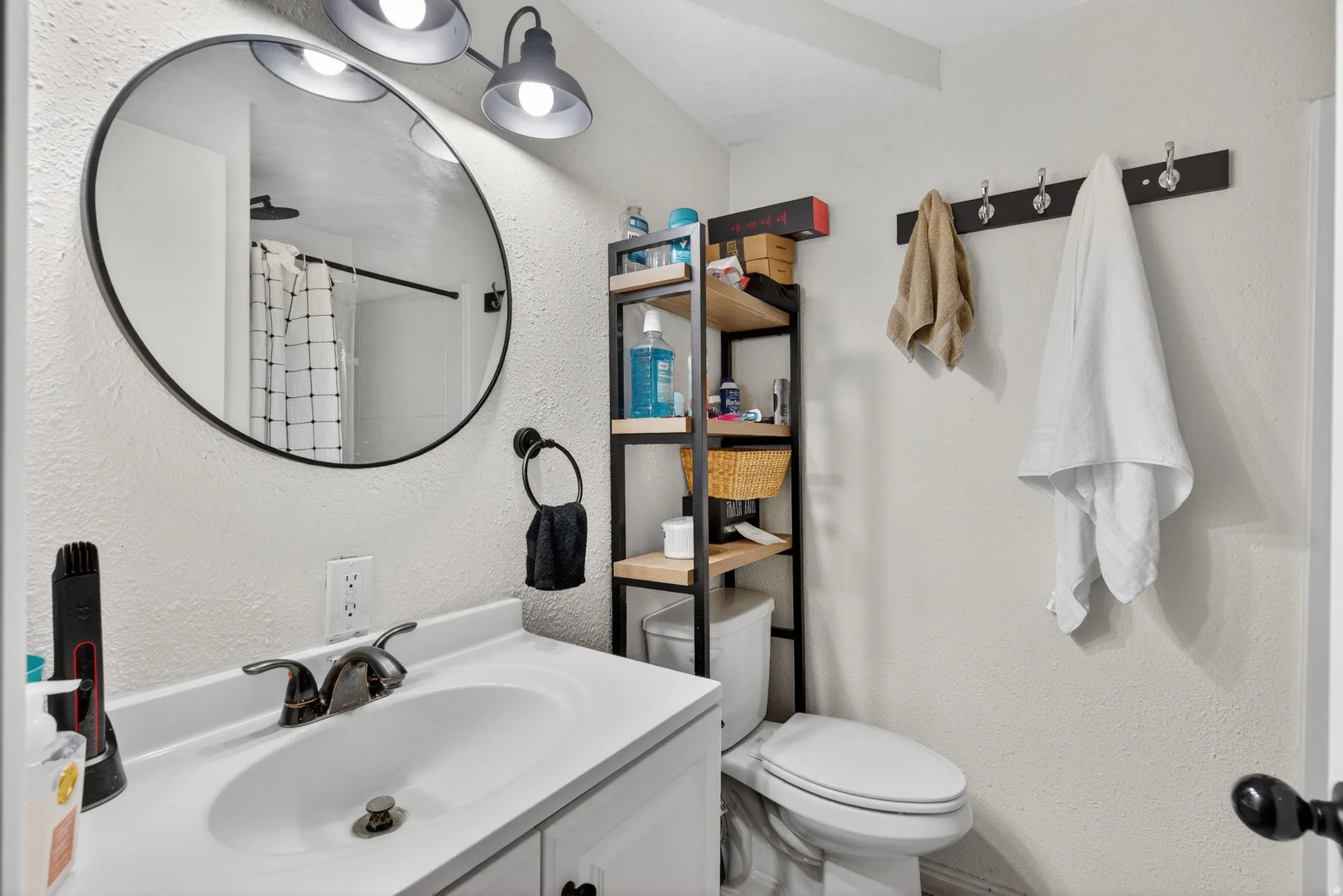 Bathroom featuring a white vanity with an undermount sink and two-handle faucet, a circular mirror with a black frame, and a three-light vanity fixture