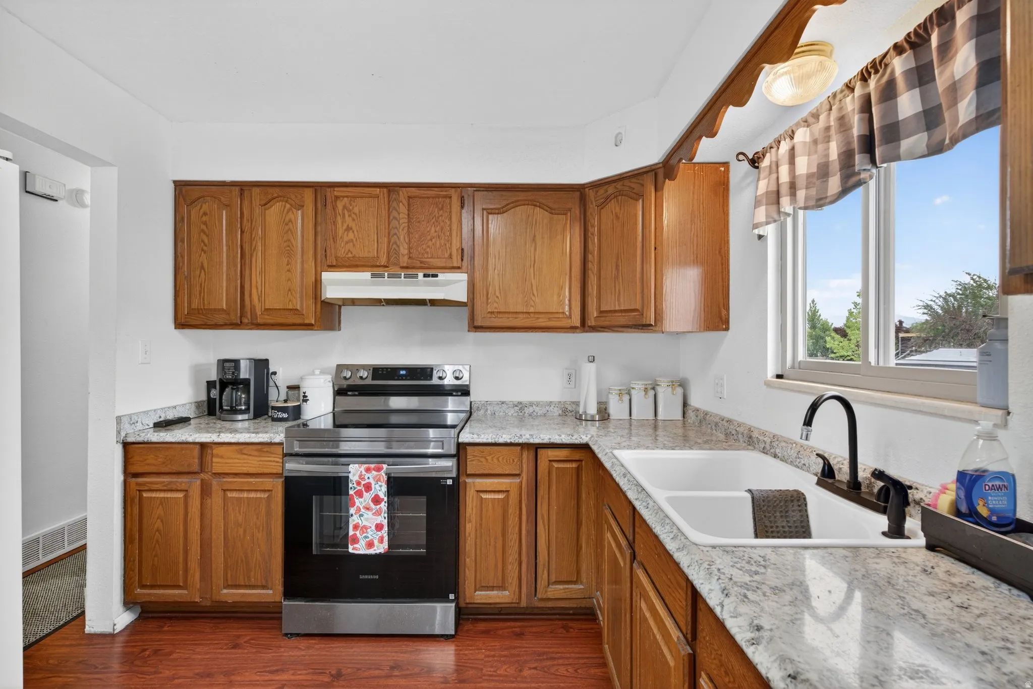 Kitchen featuring wood cabinetry, light-toned countertops, a built-in stainless steel range, and a dual basin sink with a black faucet