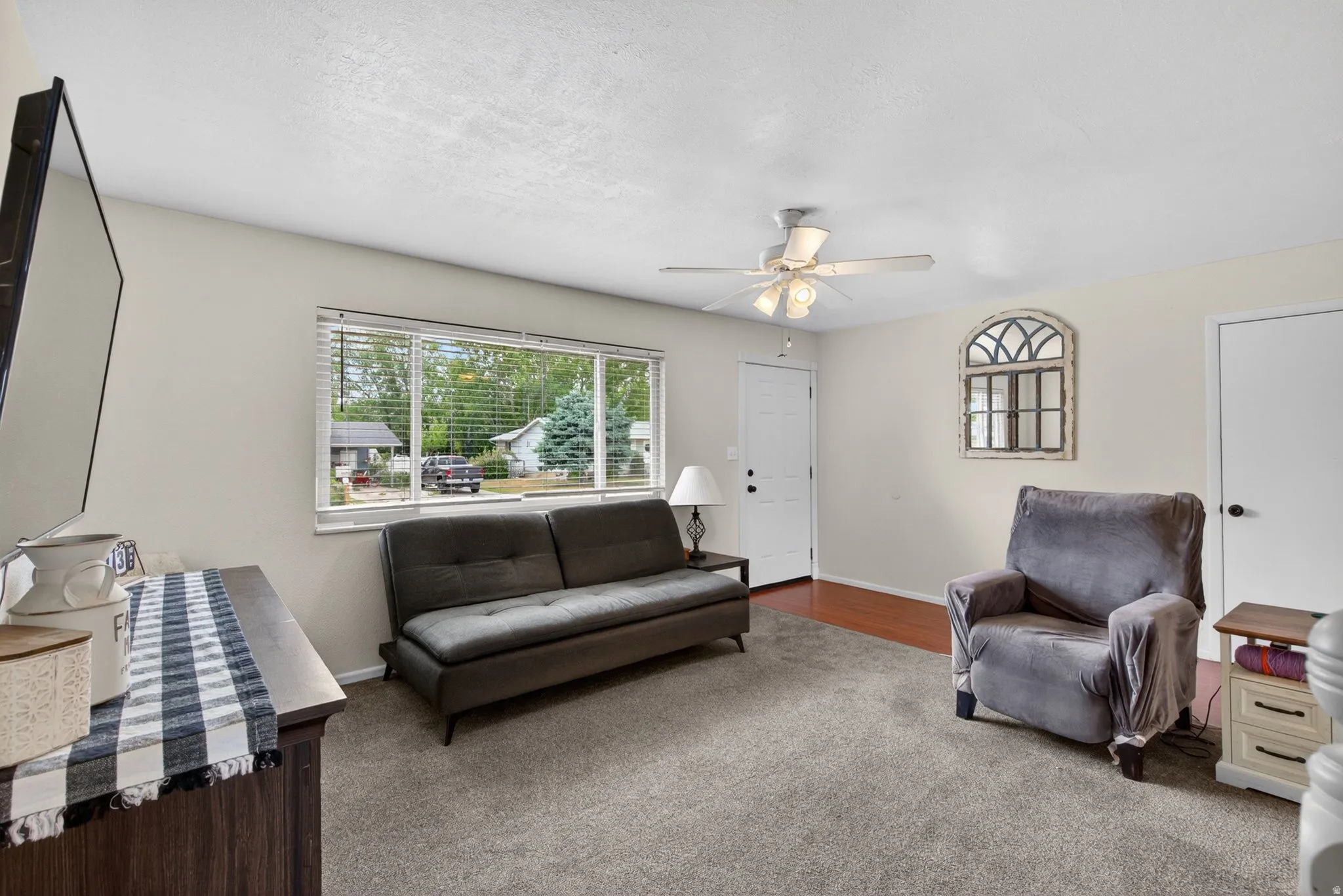 Living area featuring a ceiling fan with integrated lighting, wood-finish flooring, and a large window with blinds