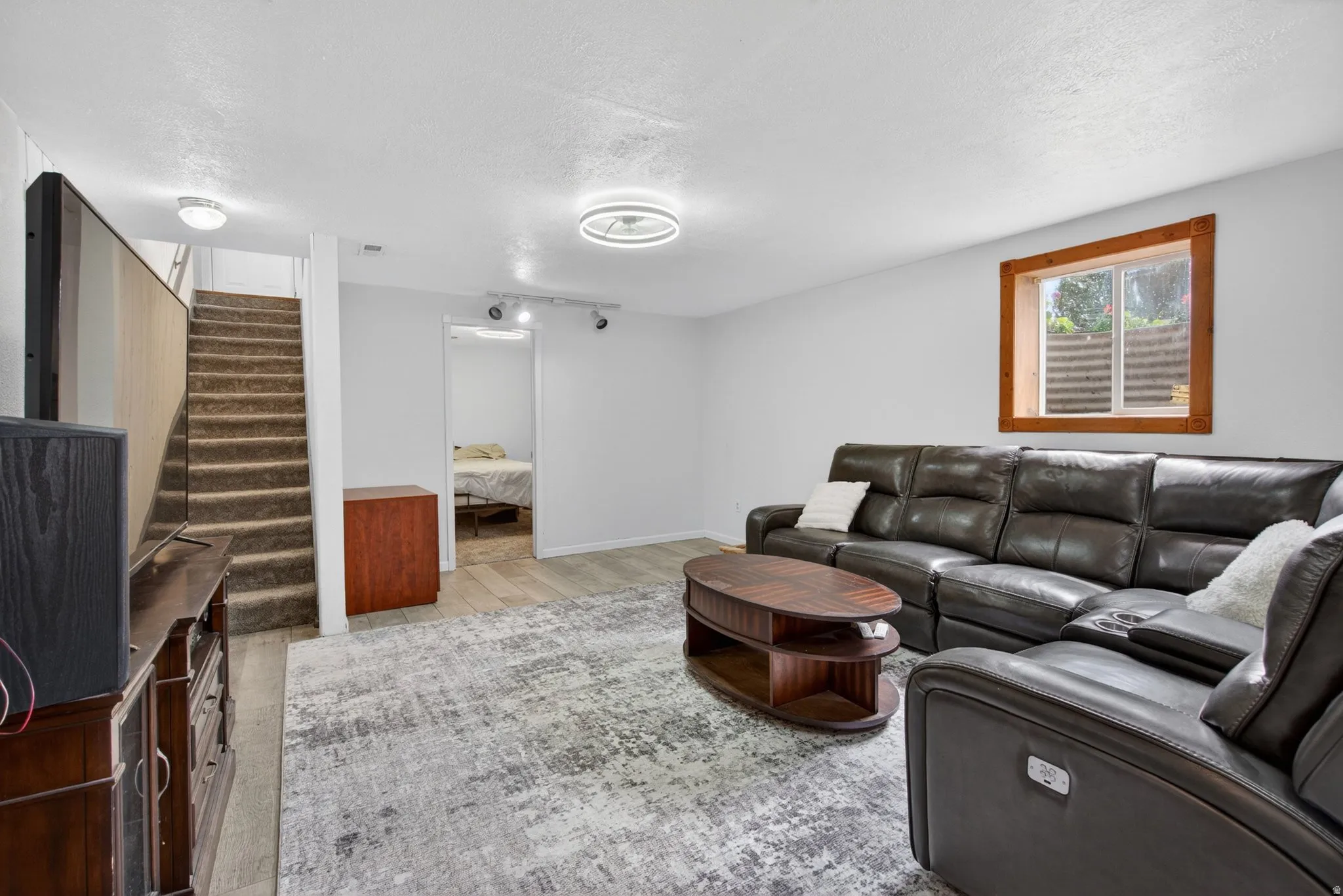 Open concept living space featuring light gray walls, wood-finish flooring, recessed lighting, and a window with wood trim