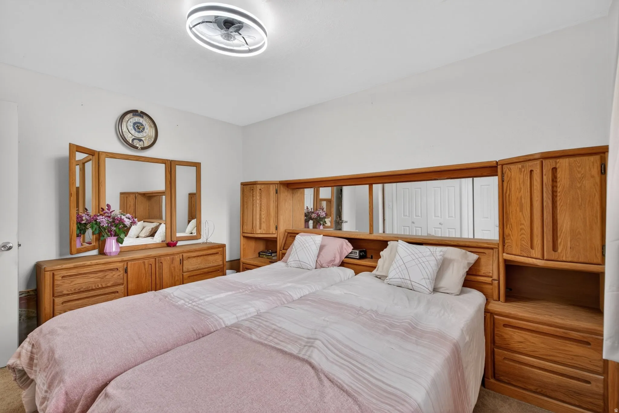 White walls with a ceiling-mounted light fixture, featuring a built-in wooden headboard with mirrored panels and integrated storage cabinetry