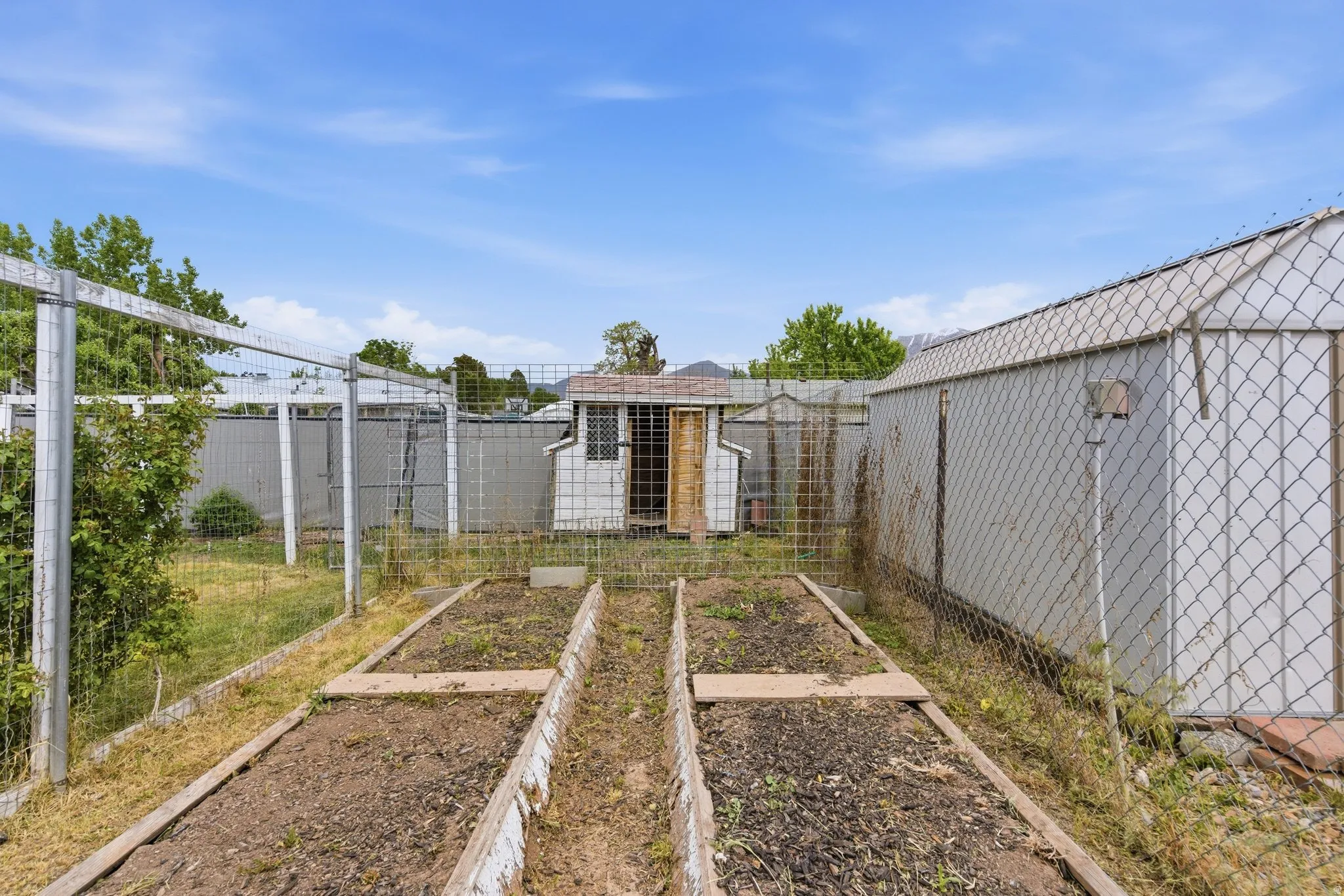 Fenced backyard with raised garden beds, chicken coop, and storage sheds