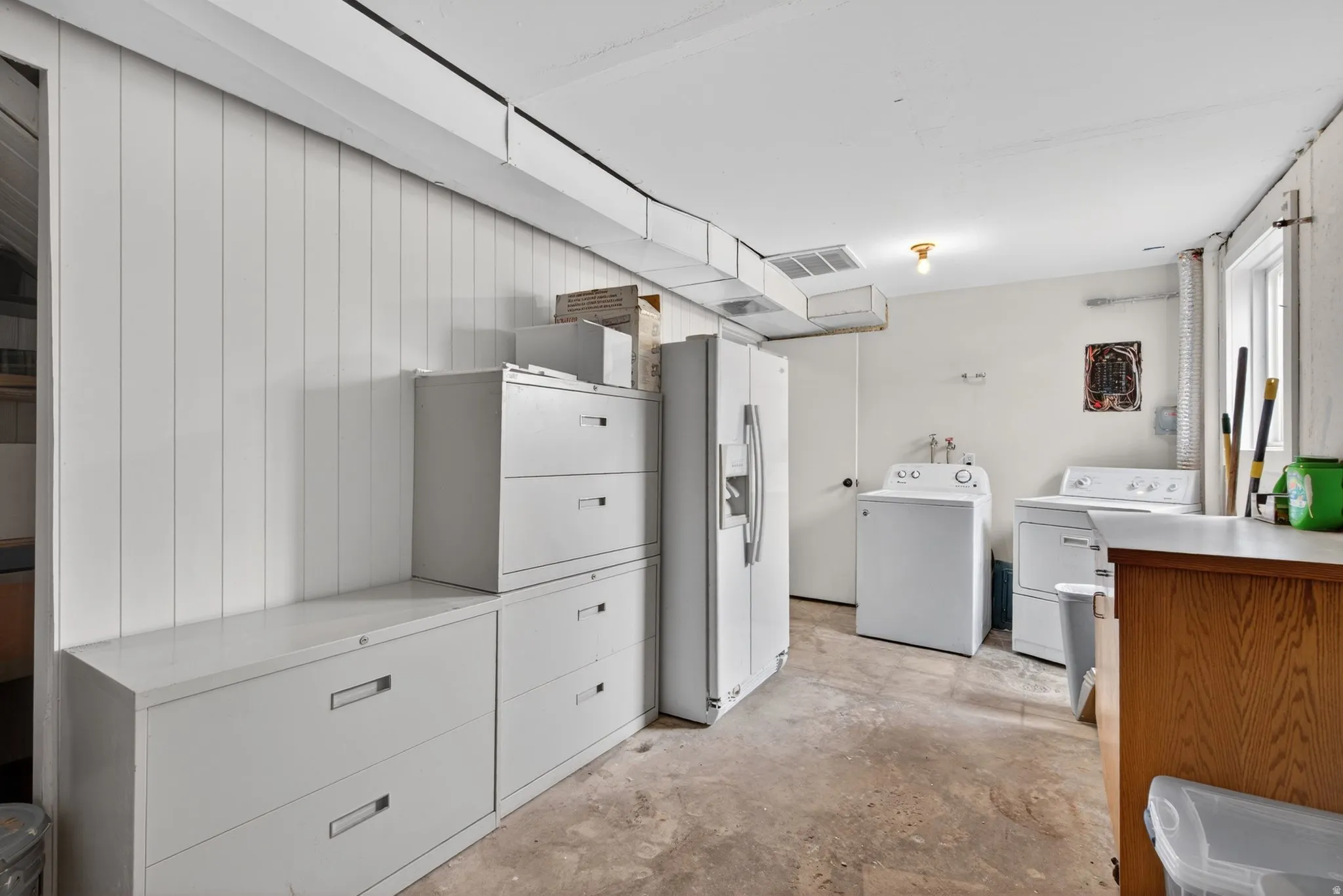 Utility area featuring white paneled walls, concrete flooring, and an exposed ceiling